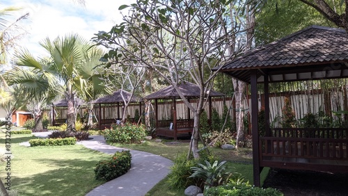 A path leads through a tropical garden with four wooden gazebos. 