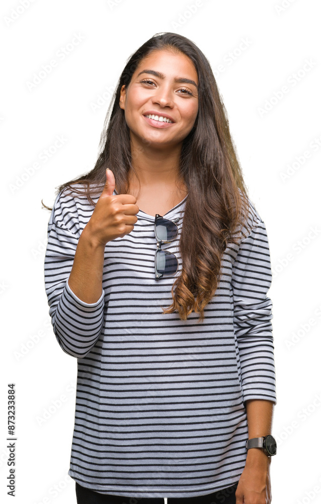 Young beautiful arab woman wearing sunglasses over isolated background doing happy thumbs up gesture with hand. Approving expression looking at the camera with showing success. Young beautiful arab woman wearing sunglasses over isolated background doing happy thumbs up gesture with hand. Approving expression looking at the camera with showing success.