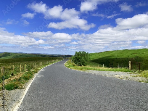 Spectacular green Welsh landscape, asphalt roadway through the rural area in Wales. Blue sky and clouds. photo