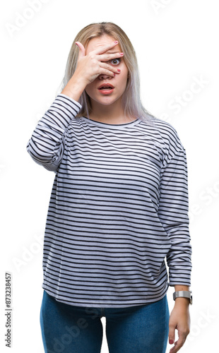 Young blonde woman over isolated background peeking in shock covering face and eyes with hand, looking through fingers with embarrassed expression.