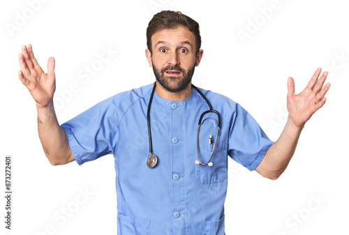 Hispanic male nurse in studio receiving a pleasant surprise, excited and raising hands.