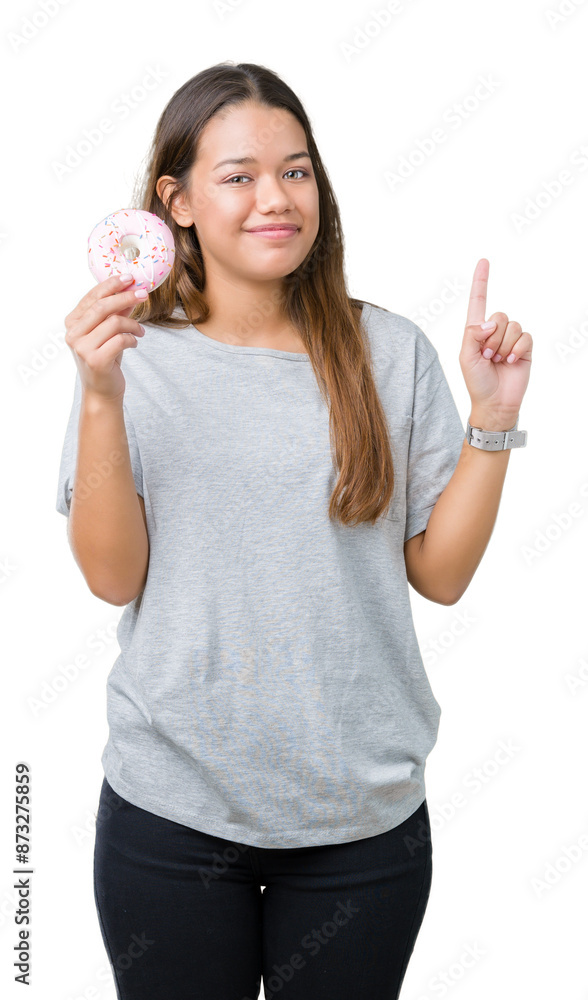 Young beautiful woman eating pink donut over isolated background surprised with an idea or question pointing finger with happy face, number one Young beautiful woman eating pink donut over isolated background surprised with an idea or question pointing finger with happy face, number one