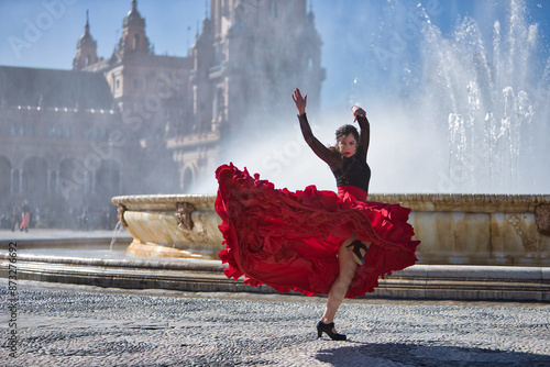 Young, beautiful, brunette woman in black shirt and red skirt, dancing flamenco in front of a beautiful fountain in Spain square in Seville. Flamenco concept, dance, art, typical Spanish. photo