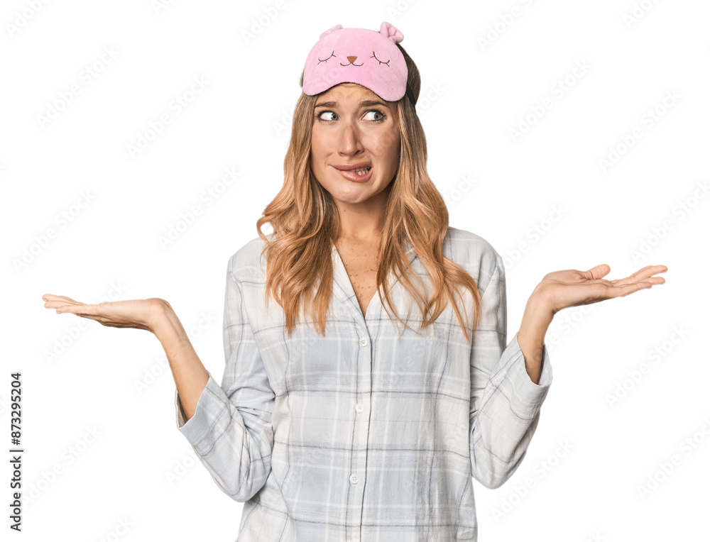 Blonde in pajamas with sleep mask confused and doubtful shrugging shoulders to hold a copy space. Blonde in pajamas with sleep mask confused and doubtful shrugging shoulders to hold a copy space.