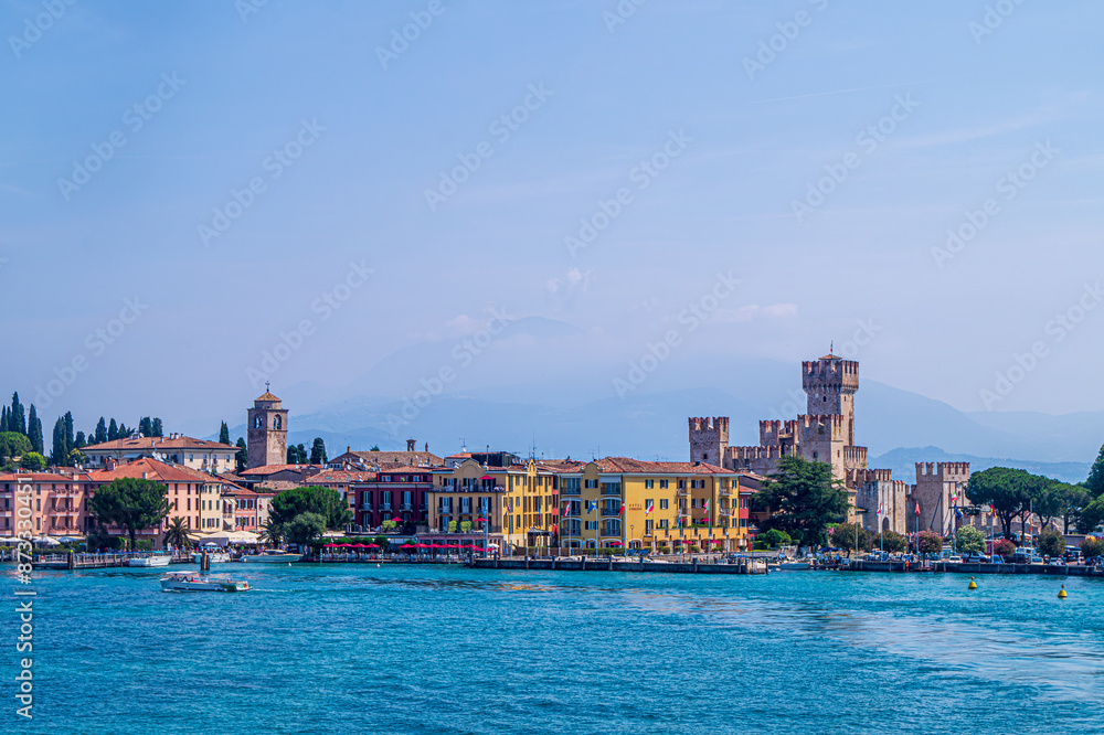 A view of Sirmione on Lake Garda taken from a ferry as it crosses the lake. Taken on a sunny day, the bright sun brings out the vibrant colours of the buildings and water A view of Sirmione on Lake Garda taken from a ferry as it crosses the lake. Taken on a sunny day, the bright sun brings out the vibrant colours of the buildings and water