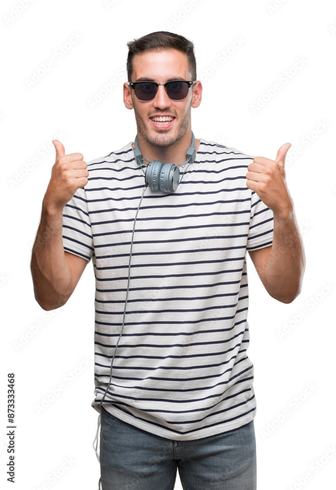 Handsome young man wearing headphones success sign doing positive gesture with hand, thumbs up smiling and happy. Looking at the camera with cheerful expression, winner gesture. Handsome young man wearing headphones success sign doing positive gesture with hand, thumbs up smiling and happy. Looking at the camera with cheerful expression, winner gesture.