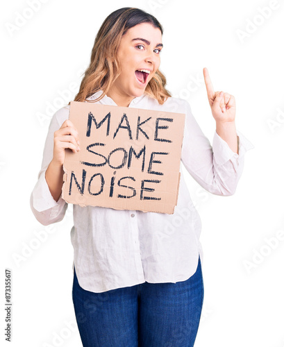 Young caucasian woman holding make some noise banner surprised with an idea or question pointing finger with happy face, number one photo