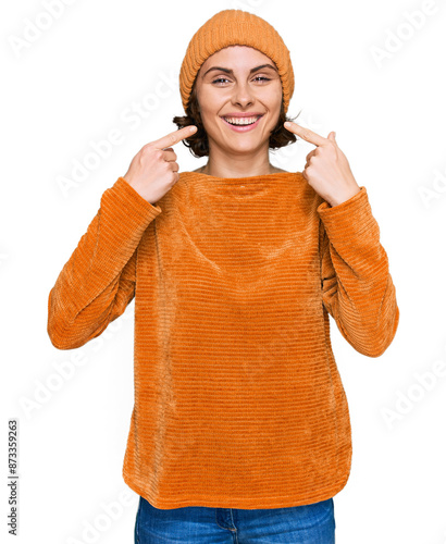 Young hispanic woman wearing casual clothes and wool cap smiling cheerful showing and pointing with fingers teeth and mouth. dental health concept.