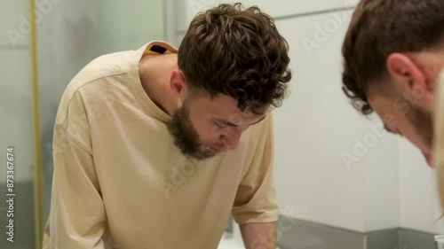 Young Caucasian bearded man in the bathroom, spitting water after brushing his teeth. Dental hygiene.