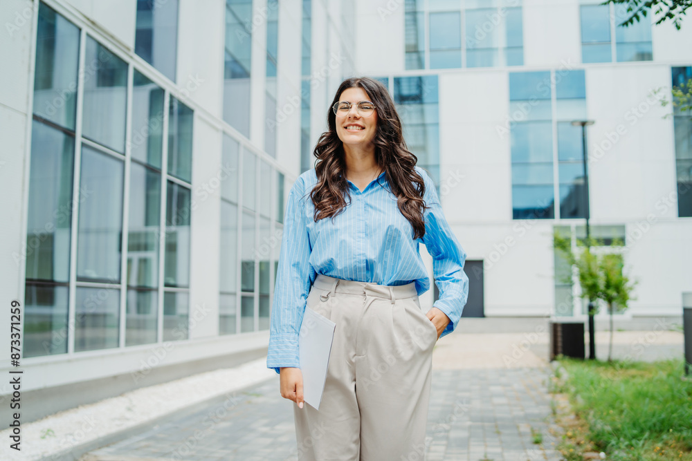 One beautiful young successful business woman going to work at business office modern building while holding papers and wearing glasses One beautiful young successful business woman going to work at business office modern building while holding papers and wearing glasses