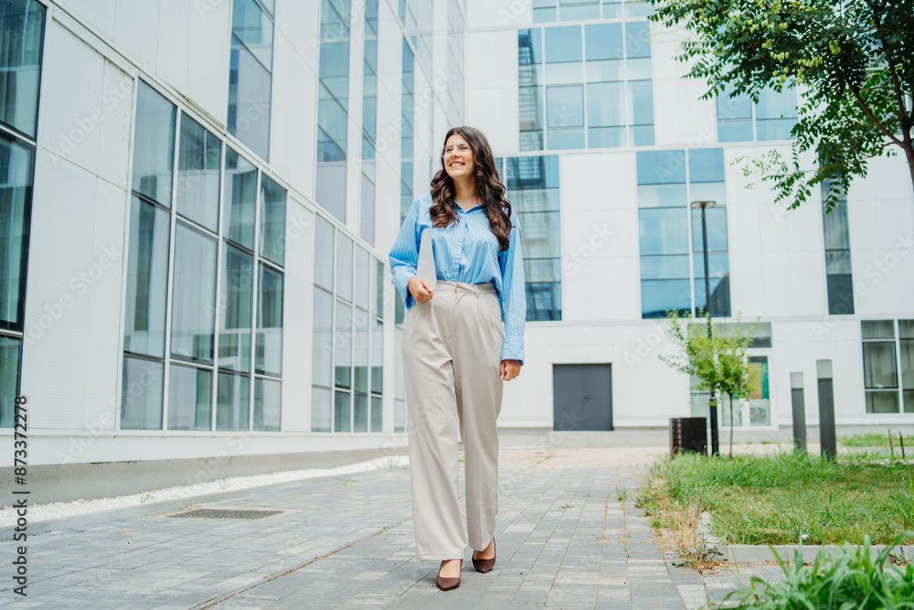 One beautiful young successful business woman going to work at business office modern building while holding papers and wearing glasses One beautiful young successful business woman going to work at business office modern building while holding papers and wearing glasses