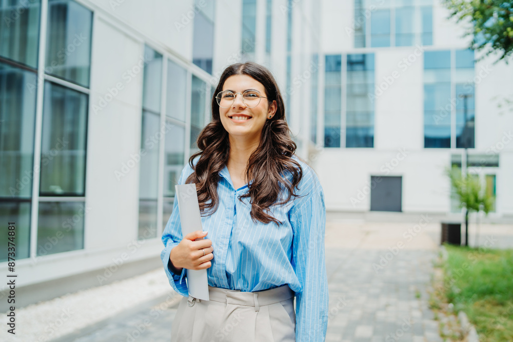 One beautiful young successful business woman going to work at business office modern building while holding papers and wearing glasses One beautiful young successful business woman going to work at business office modern building while holding papers and wearing glasses