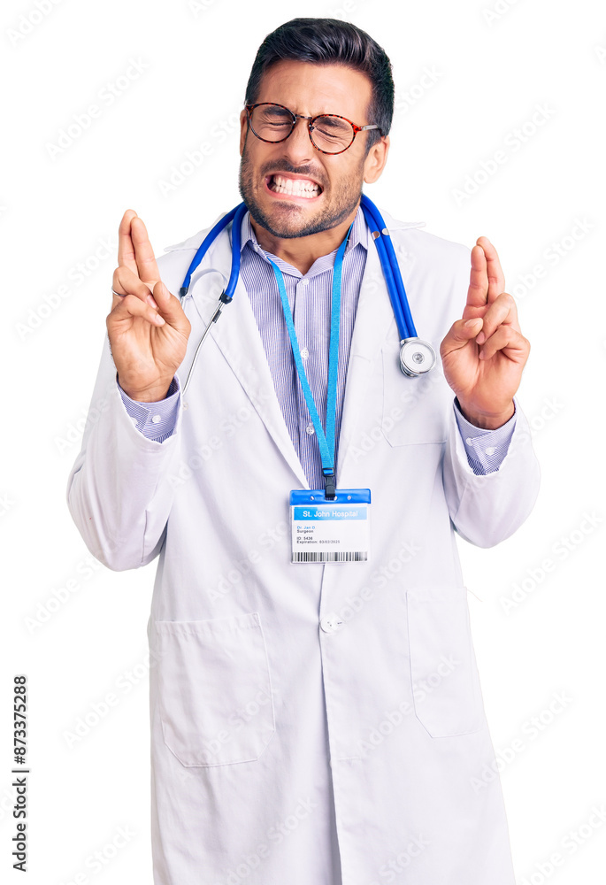 Young hispanic man wearing doctor uniform and stethoscope gesturing finger crossed smiling with hope and eyes closed. luck and superstitious concept. Young hispanic man wearing doctor uniform and stethoscope gesturing finger crossed smiling with hope and eyes closed. luck and superstitious concept.