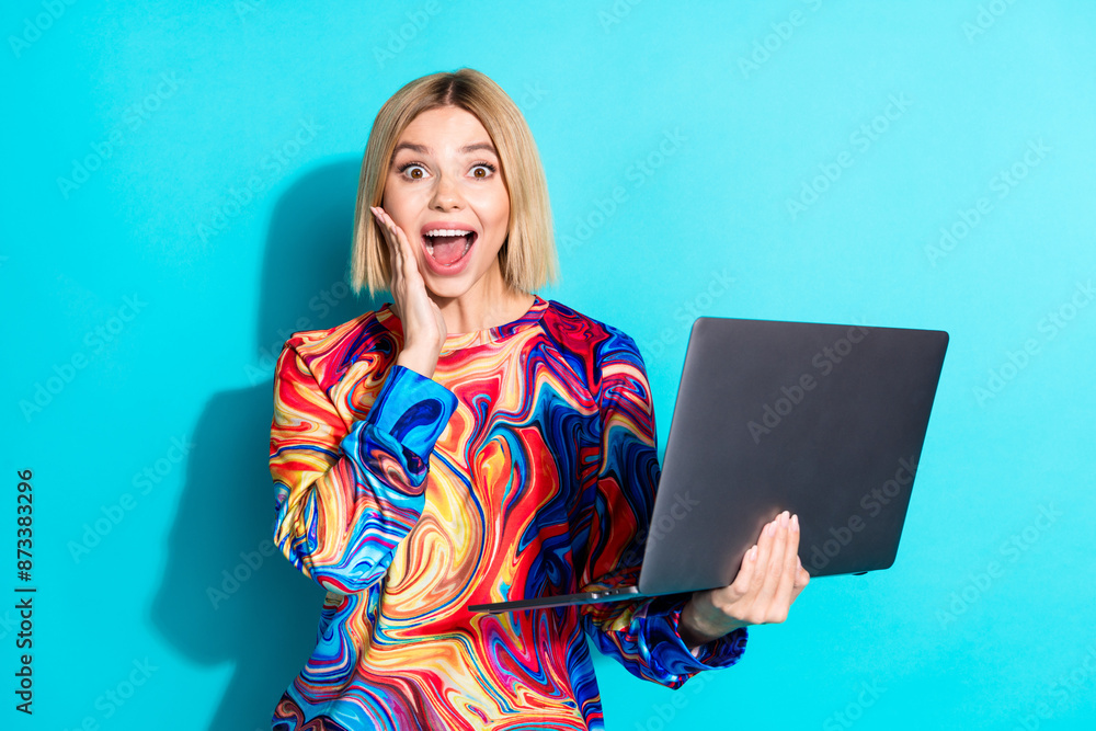 Photo of impressed overjoyed girl with bob hairstyle dressed print shirt holding laptop in hands isolated on blue color background