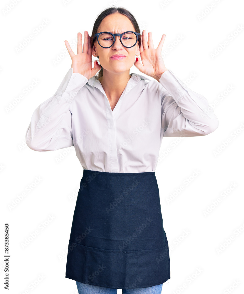 Beautiful brunette young woman wearing professional waitress apron trying to hear both hands on ear gesture, curious for gossip. hearing problem, deaf Beautiful brunette young woman wearing professional waitress apron trying to hear both hands on ear gesture, curious for gossip. hearing problem, deaf