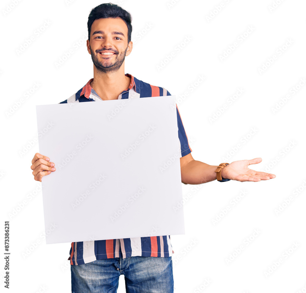 Young handsome hispanic man holding cardboard banner with blank space celebrating victory with happy smile and winner expression with raised hands Young handsome hispanic man holding cardboard banner with blank space celebrating victory with happy smile and winner expression with raised hands