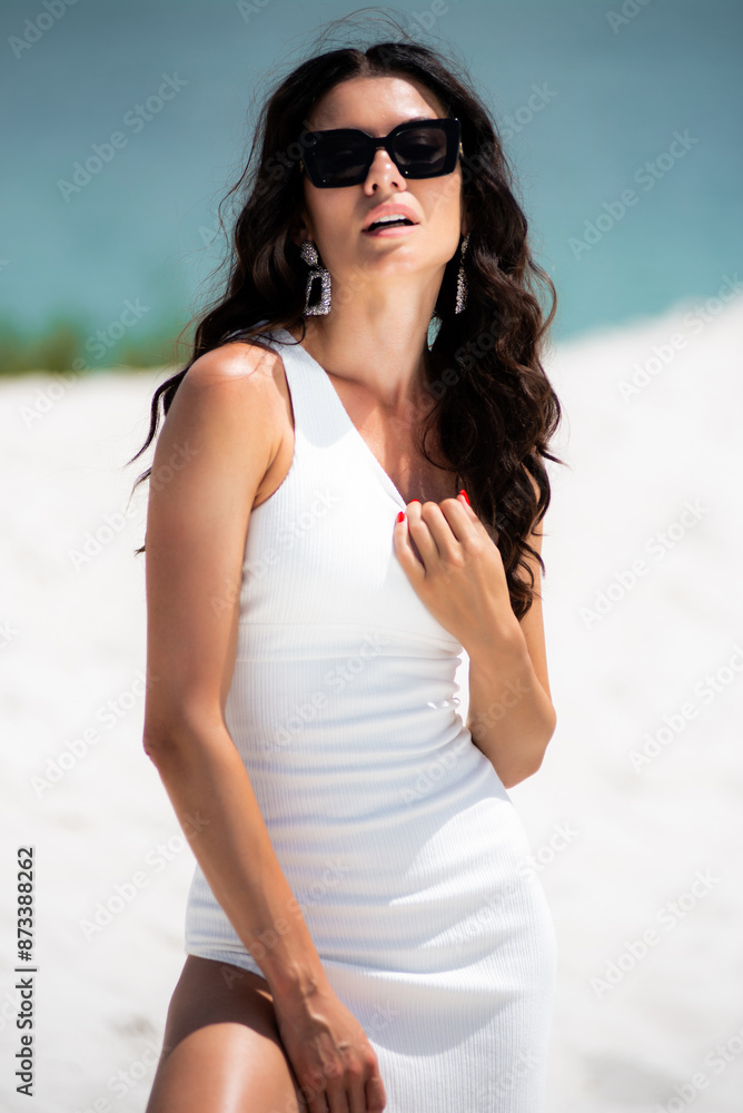 Luxury fashion woman in white dress and sunglasses on the white sand beach Luxury fashion woman in white dress and sunglasses on the white sand beach
