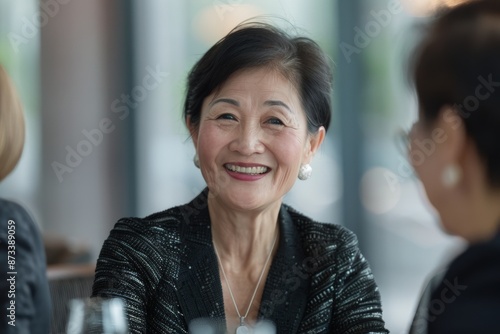 An elegant woman in sophisticated attire is joyously smiling while engaging in a friendly conversation at a social gathering, exhibiting warmth and elegance. © ChaoticMind