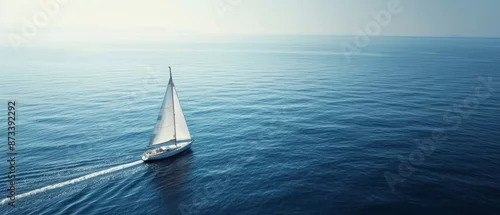 Obraz  z motywem A sailboat with white sails navigates the calm, expansive blue sea under a clear sky, creating a serene and peaceful atmosphere