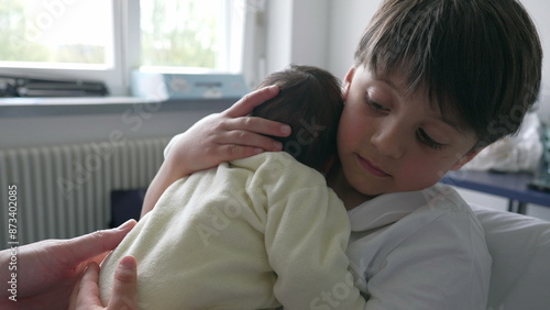 Older sibling tenderly holding and comforting newborn baby in a yellow onesie, highlighting the loving bond and gentle interaction between siblings in early days of family life