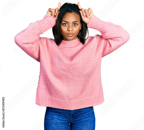 Beautiful hispanic woman wearing casual winter sweater doing funny gesture with finger over head as bull horns