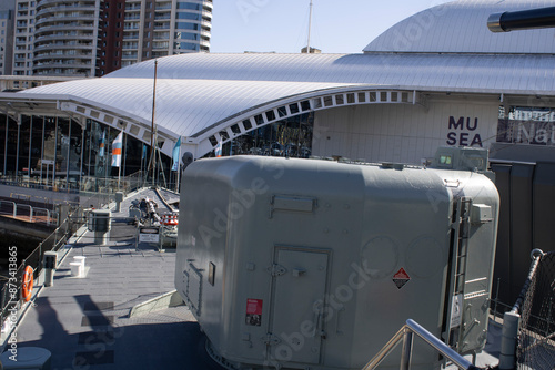 Capturing the majestic strength of an Australian naval warship in Sydney's sea, this strikingphoto features the formidable back of a cannon against the backdrop of Sydney's iconic cityscape. 