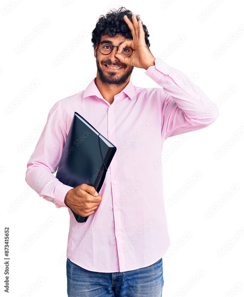 © Krakenimages.com - Handsome young man with curly hair and bear holding business folder smiling happy doing ok sign with hand on eye looking through fingers