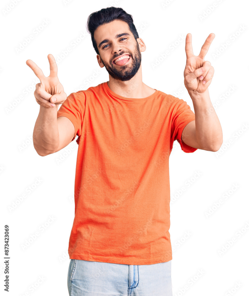 Young handsome man with beard wearing casual t-shirt smiling with tongue out showing fingers of both hands doing victory sign. number two. Young handsome man with beard wearing casual t-shirt smiling with tongue out showing fingers of both hands doing victory sign. number two.