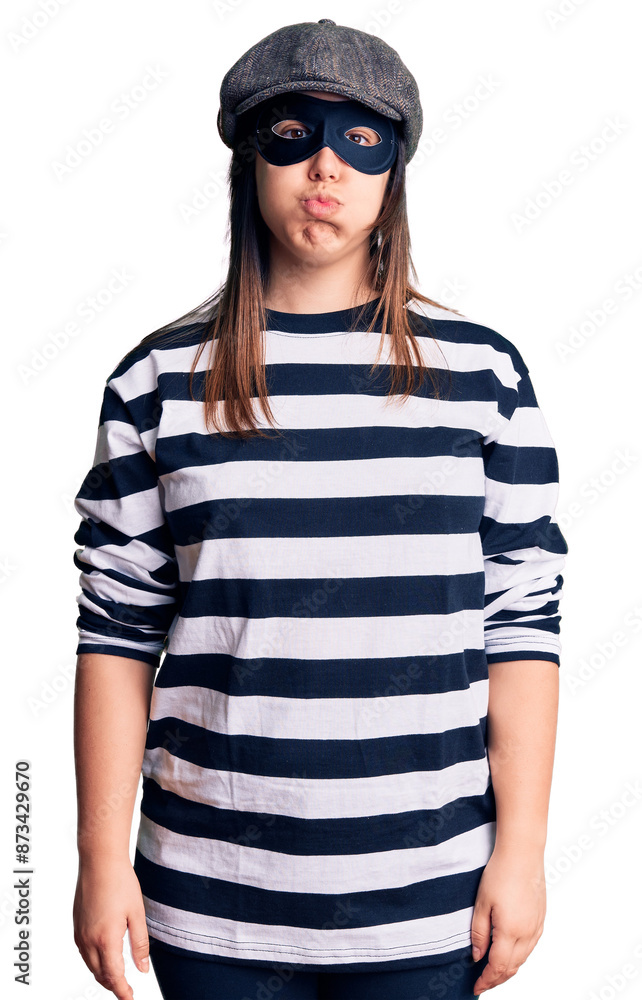 Young beautiful brunette woman wearing burglar mask puffing cheeks with funny face. mouth inflated with air, crazy expression. Young beautiful brunette woman wearing burglar mask puffing cheeks with funny face. mouth inflated with air, crazy expression.