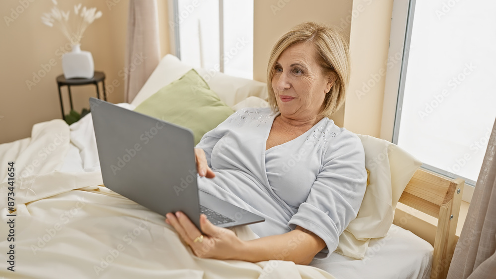 Caucasian middle-aged woman relaxing with a laptop in a bright bedroom at home Caucasian middle-aged woman relaxing with a laptop in a bright bedroom at home
