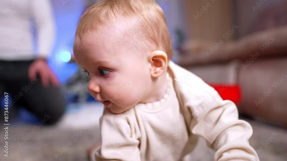 Adorable little toddler crawls by the floor approaching camera. A red cake is shown to baby, distracting him for a moment. Close up. Unrecognized man sits on the floor at backdrop. Adorable little toddler crawls by the floor approaching camera. A red cake is shown to baby, distracting him for a moment. Close up. Unrecognized man sits on the floor at backdrop.