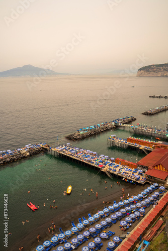 Obraz na płótnie Sorrento, Italy - July 24, 2024: People relaxing on the beach on the pier and swimming in the sea on inflatable air beds in Sorrento and boats floating against mount vesuvius volcano w salonie