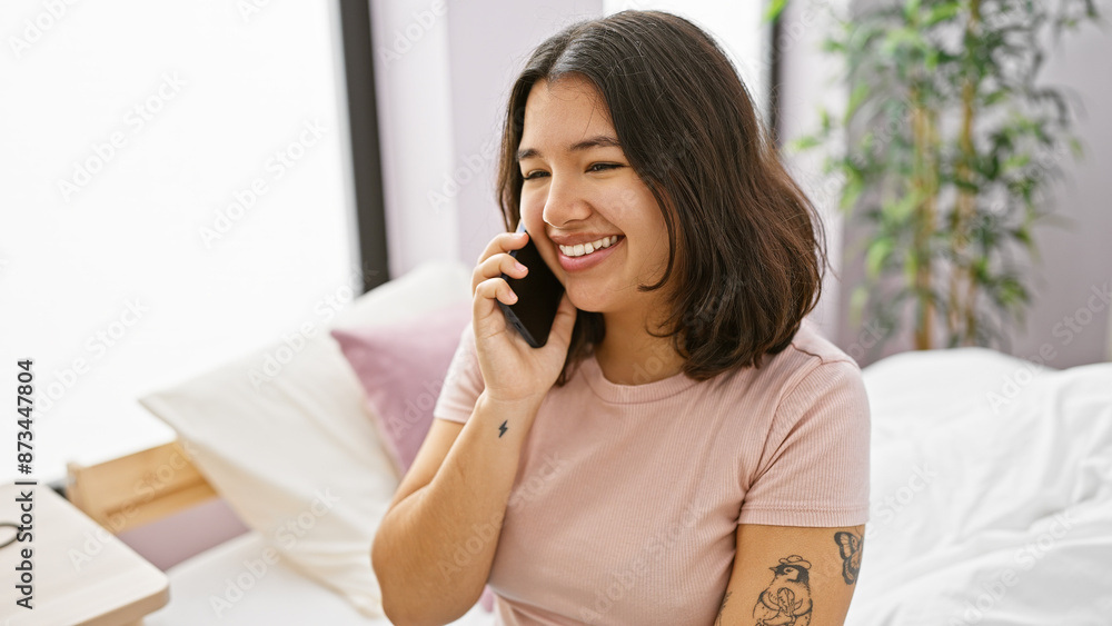 Smiling hispanic woman talking on phone in a cozy bedroom setting Smiling hispanic woman talking on phone in a cozy bedroom setting
