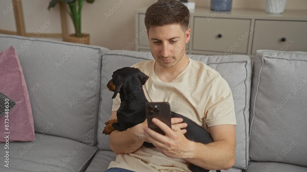 Young hispanic man holds his dachshund dog while looking at his phone in a cozy living room, reflecting a typical indoor moment in an apartment. Young hispanic man holds his dachshund dog while looking at his phone in a cozy living room, reflecting a typical indoor moment in an apartment.