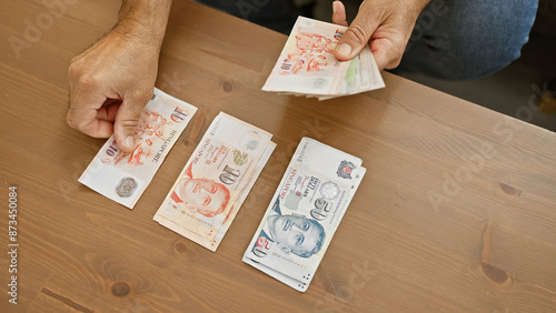 Photography Man counts singaporean currency at wooden table indoors, providing a domestic fi