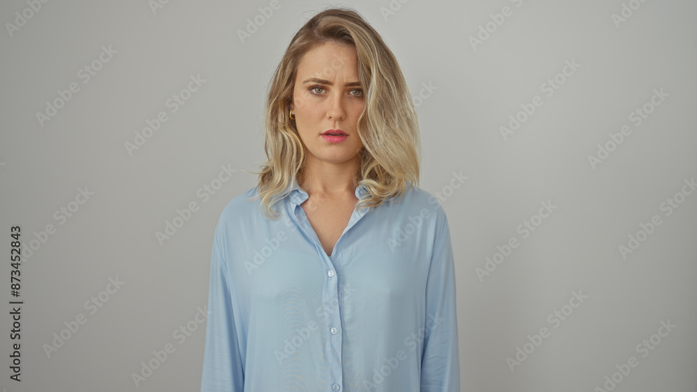 Portrait of a young, beautiful, blonde woman in a blue shirt standing against a white background, conveying a thoughtful expression. Portrait of a young, beautiful, blonde woman in a blue shirt standing against a white background, conveying a thoughtful expression.