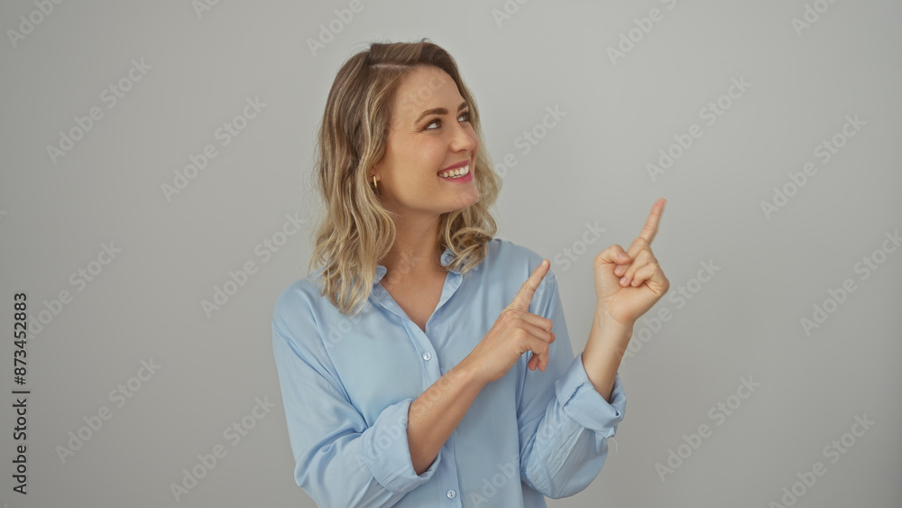 Smiling caucasian woman in blue shirt pointing upwards on a white background, exuding a friendly and casual vibe Smiling caucasian woman in blue shirt pointing upwards on a white background, exuding a friendly and casual vibe