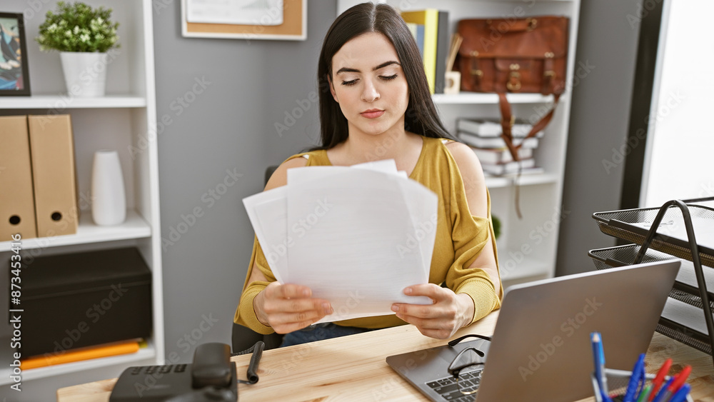 A focused hispanic woman reviews documents in her modern office, exemplifying professionalism and efficiency. A focused hispanic woman reviews documents in her modern office, exemplifying professionalism and efficiency.