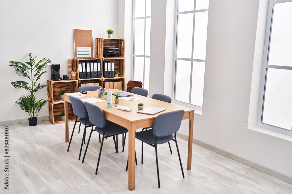 Modern office interior with a wooden table, chairs, plants, and storage shelves in a bright room with large windows. Modern office interior with a wooden table, chairs, plants, and storage shelves in a bright room with large windows.