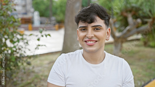 Smiling young man in white shirt posing in a lush park with blurred greenery in the background