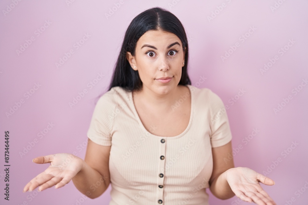 Young hispanic woman standing over pink background clueless and confused with open arms, no idea concept. Young hispanic woman standing over pink background clueless and confused with open arms, no idea concept.
