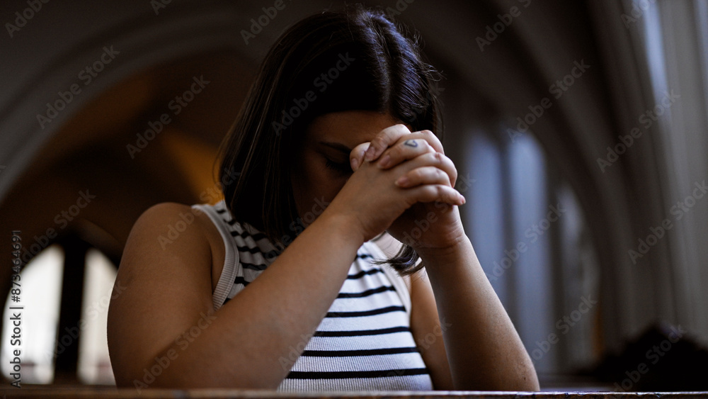Young beautiful hispanic woman praying on a church bench at Augustinian Church in Vienna Young beautiful hispanic woman praying on a church bench at Augustinian Church in Vienna