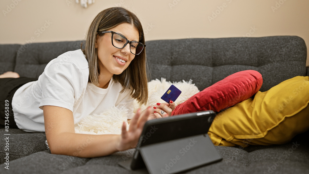 Hispanic woman with glasses using tablet and credit card for online shopping in living room Hispanic woman with glasses using tablet and credit card for online shopping in living room