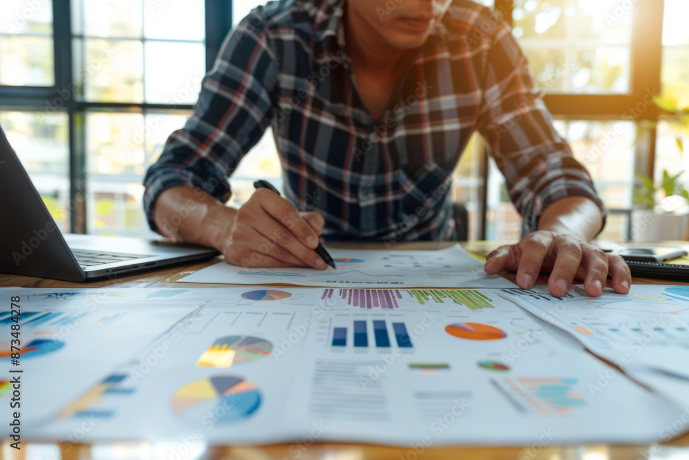 Businessman reviewing and analyzing financial charts and graphs at a desk in a bright office Businessman reviewing and analyzing financial charts and graphs at a desk in a bright office