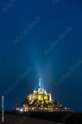 foto verticale di Mont-Saint-Michel ripreso in notturna, illuminato da due fasci di luce che si incrociano sulla sommità