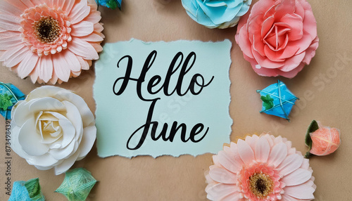 Hello June calligraphic text message written with black marker pen on recycled paper label tag with decorative floral background, cardboard, reused material flowers in peach, pink, turquoise colors. 