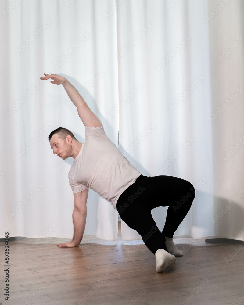Fototapeta premium Home yoga pose workouts. A man performs sports exercises with his legs and arms. Male athlete stretches.