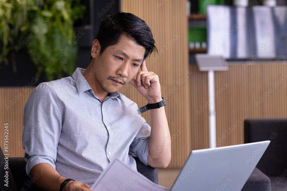 Working on laptop, man reviewing documents and concentrating in modern office Working on laptop, man reviewing documents and concentrating in modern office