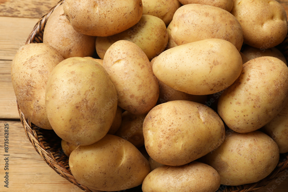 Many fresh potatoes in wicker basket on wooden table, closeup Many fresh potatoes in wicker basket on wooden table, closeup