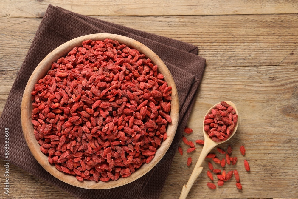 Dried goji berries in bowl and spoon on wooden table, flat lay Dried goji berries in bowl and spoon on wooden table, flat lay